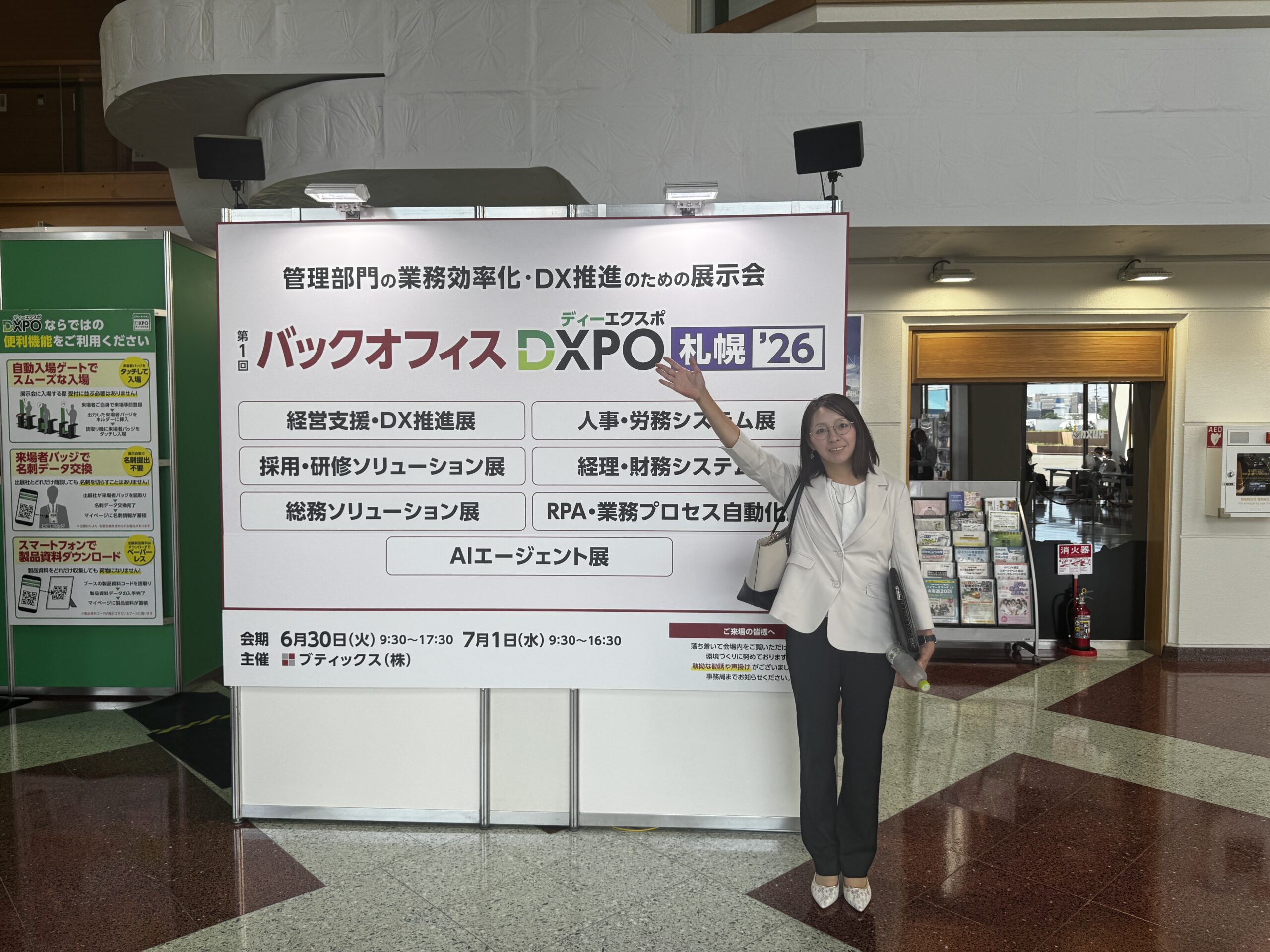 AIエージェント導入支援講師 上田良江。DXPO札幌「AIエージェント展」会場の看板前に立つ様子